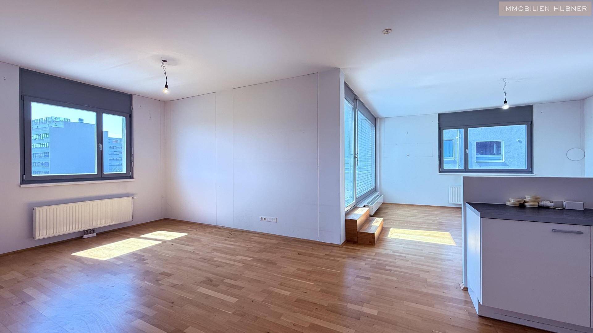 Geräumiges Wohnzimmer mit Holzboden und mehreren Fenstern, die viel Tageslicht hereinlassen.