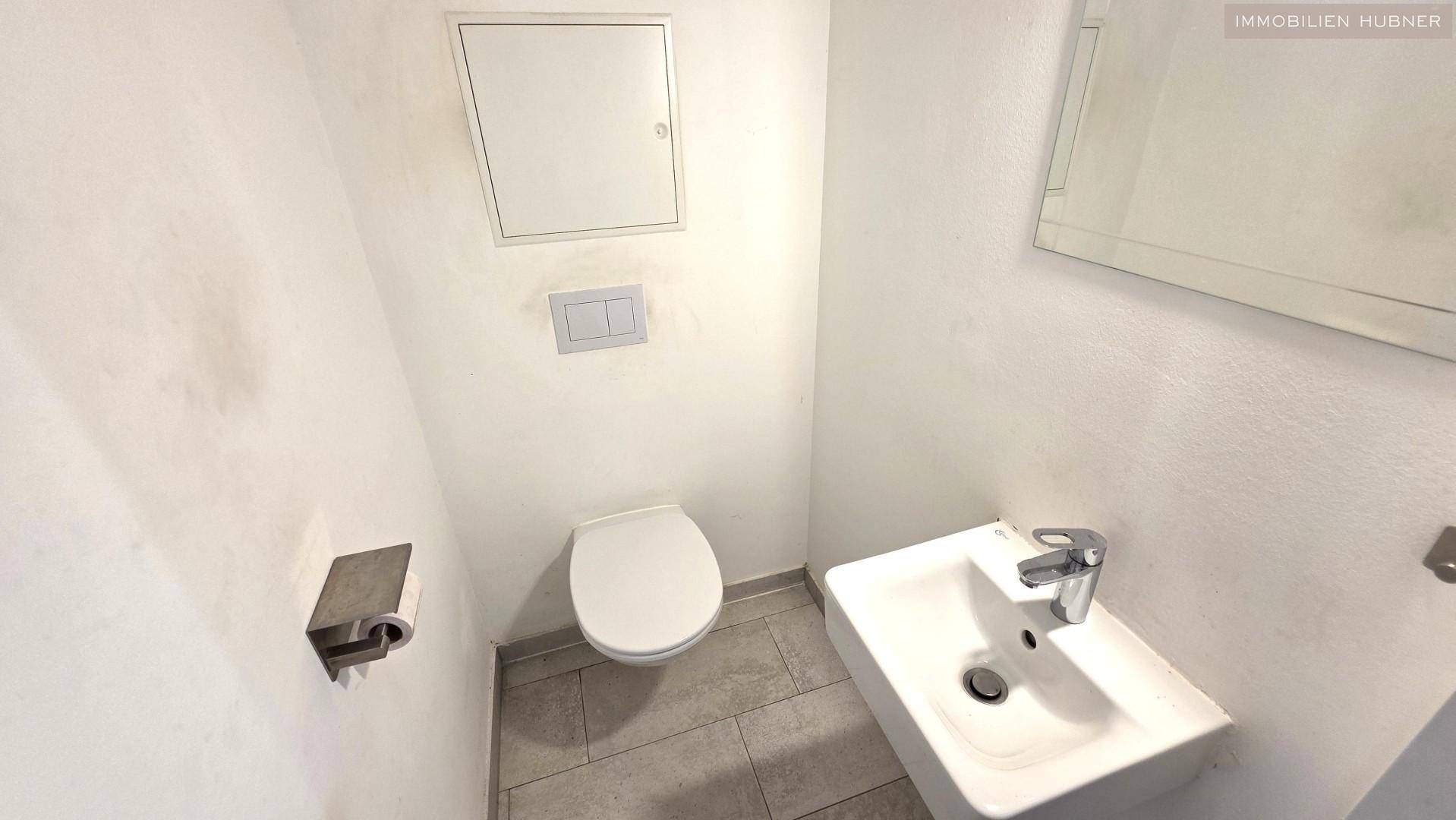 Helles Gäste-WC mit Waschbecken, Toilette und Spiegel, funktional und sauber gestaltet.