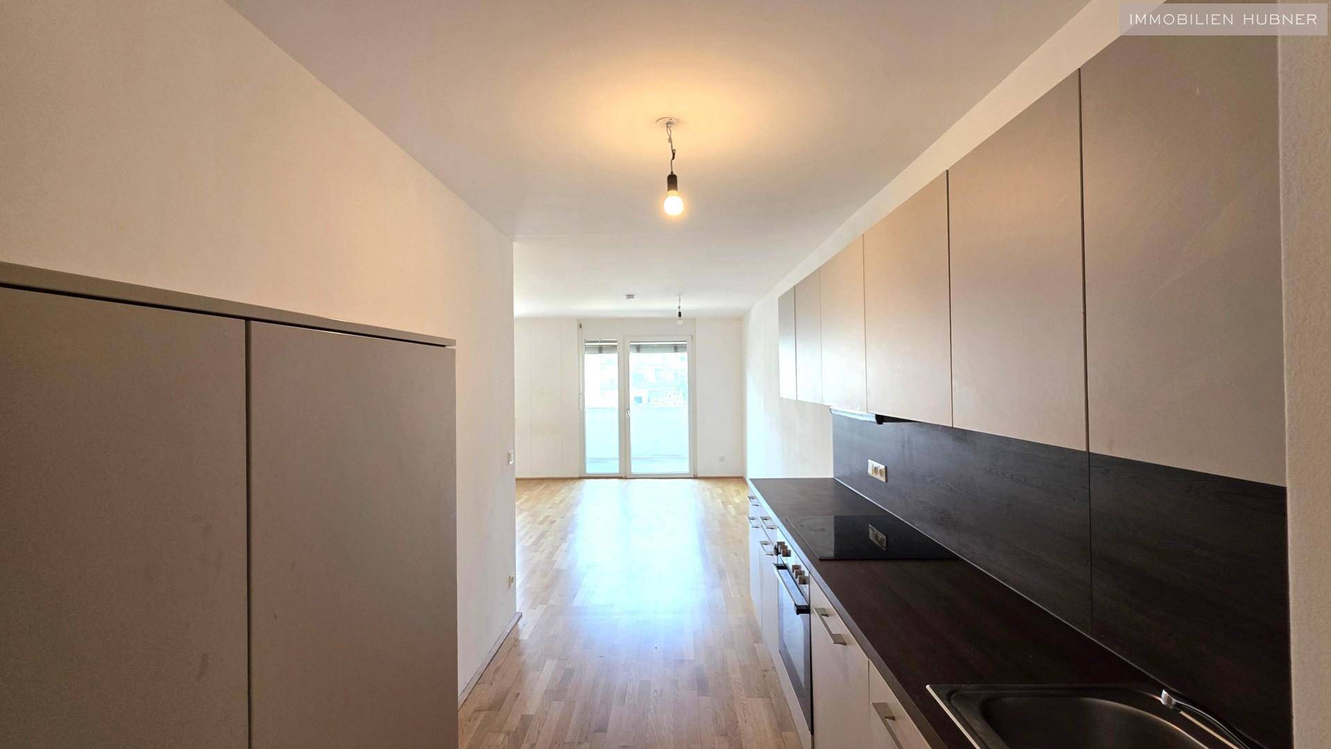 Blick von der Küche in den hellen Wohnbereich mit Parkettboden und Zugang zum Balkon.