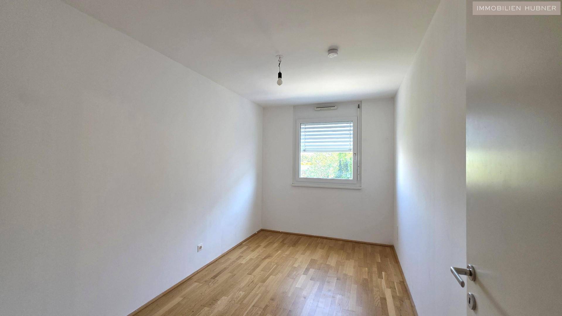 Helles Schlafzimmer mit Parkettboden und Fenster, bietet eine ruhige Atmosphäre für Erholung.