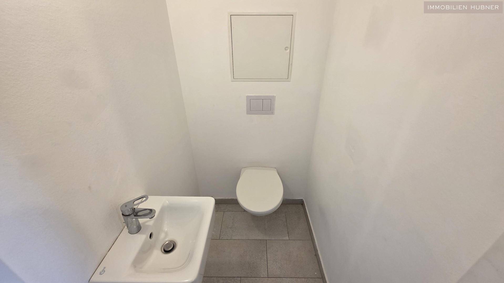 Separates WC mit Toilette, kleinem Waschbecken und modernen grauen Bodenfliesen.