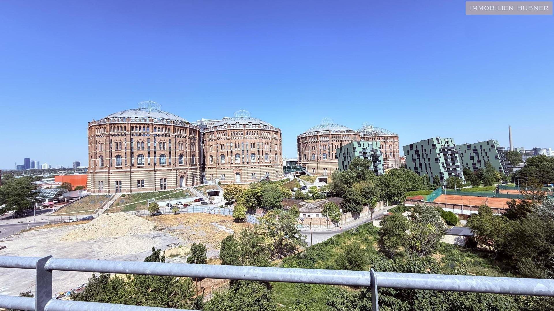 Panoramablick auf die historischen Gasometer und moderne Gebäude in der Ferne unter blauem Himmel.