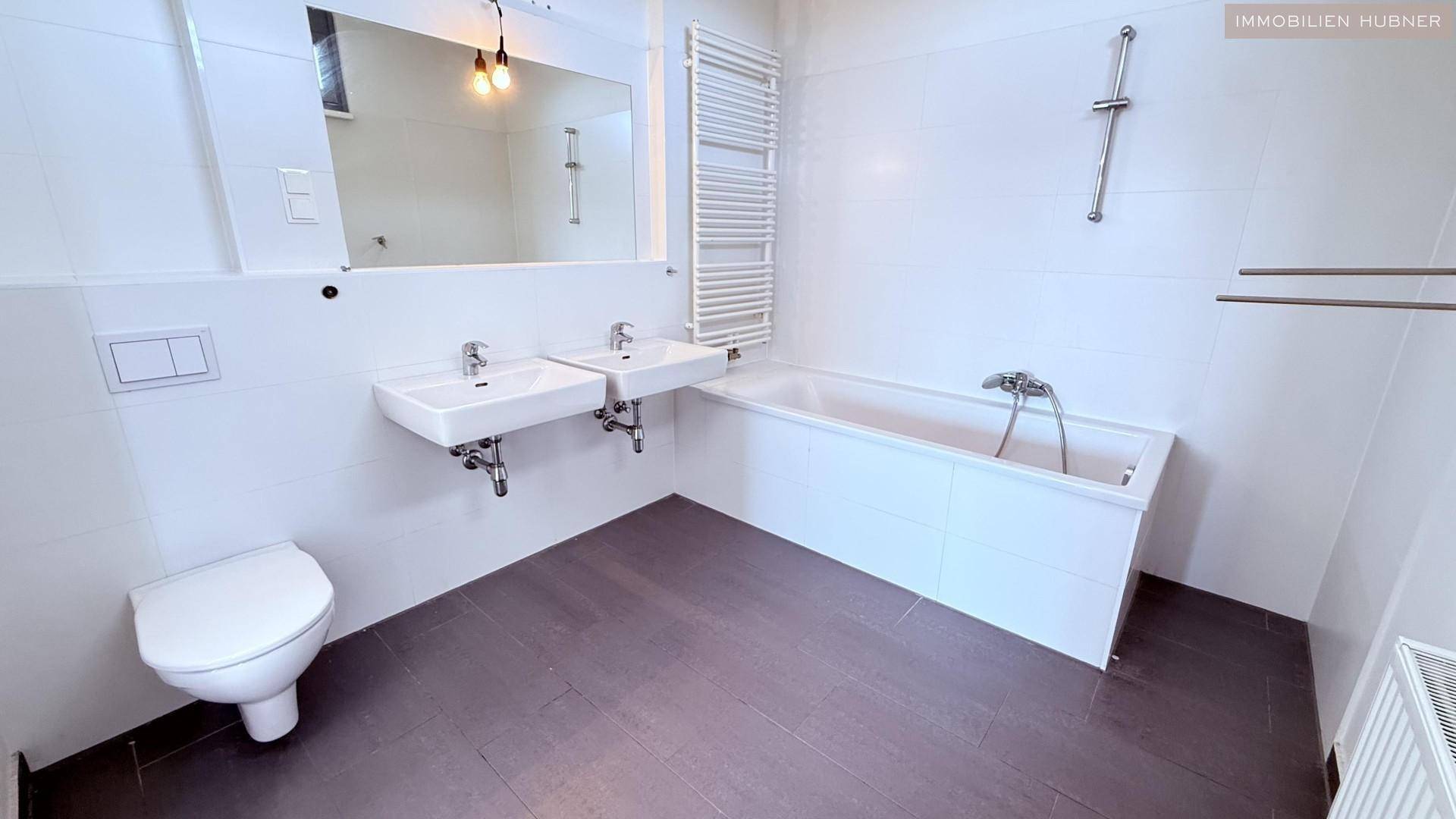 Modernes Badezimmer mit Doppelwaschbecken, Badewanne, WC und beheiztem Handtuchhalter.