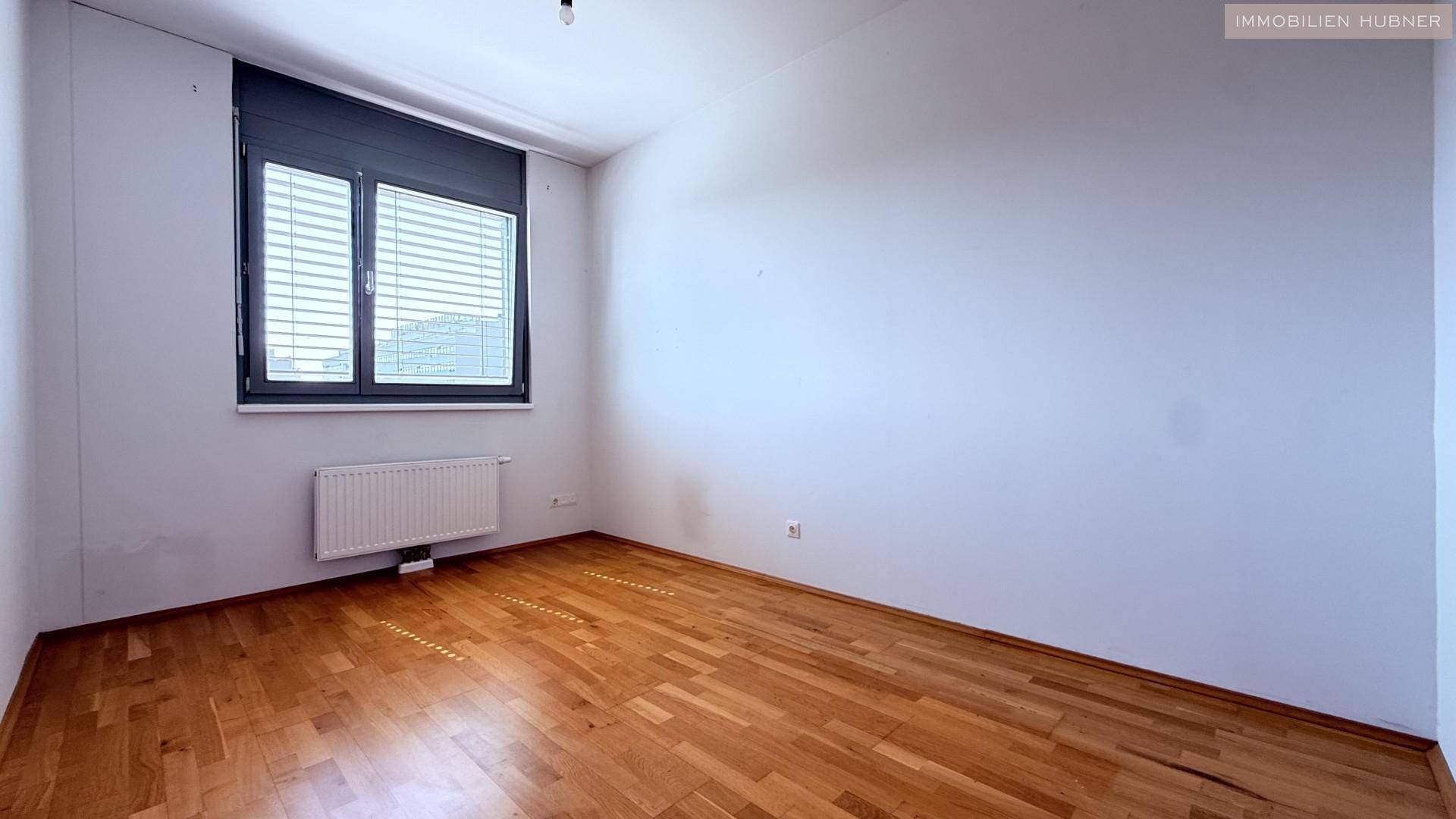 Geräumiges Zimmer mit Holzboden und Fenster, bereit zur individuellen Einrichtung.