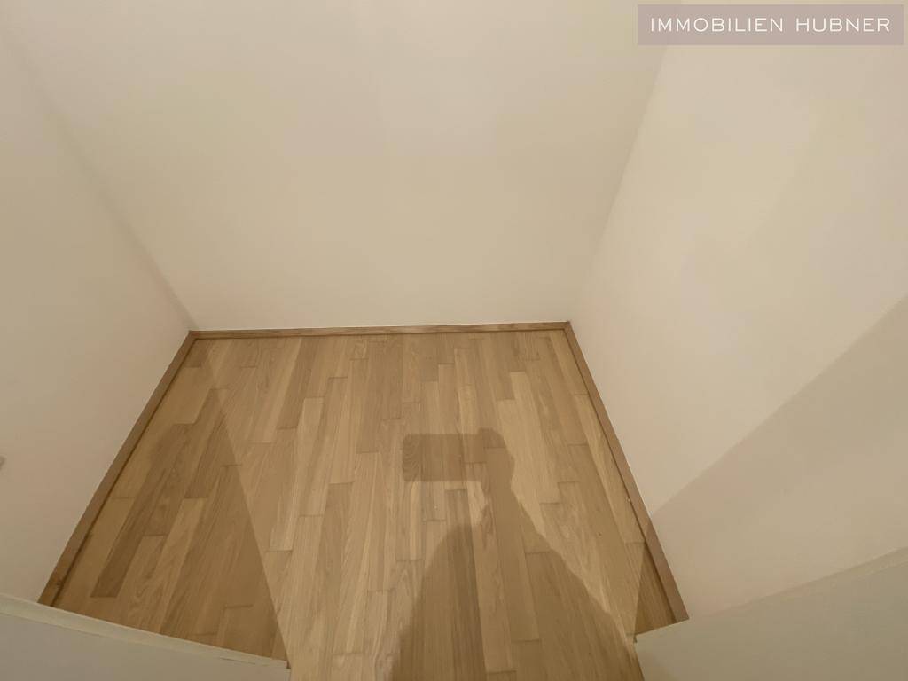 Innenraum mit hellem Parkettboden und weißen Wänden, die auf ein neues Gebäude hindeuten.