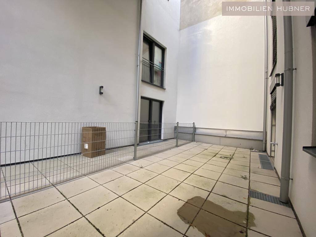 Geräumige Außenterrasse mit Fliesenboden, umgeben von modernen Gebäudefassaden.