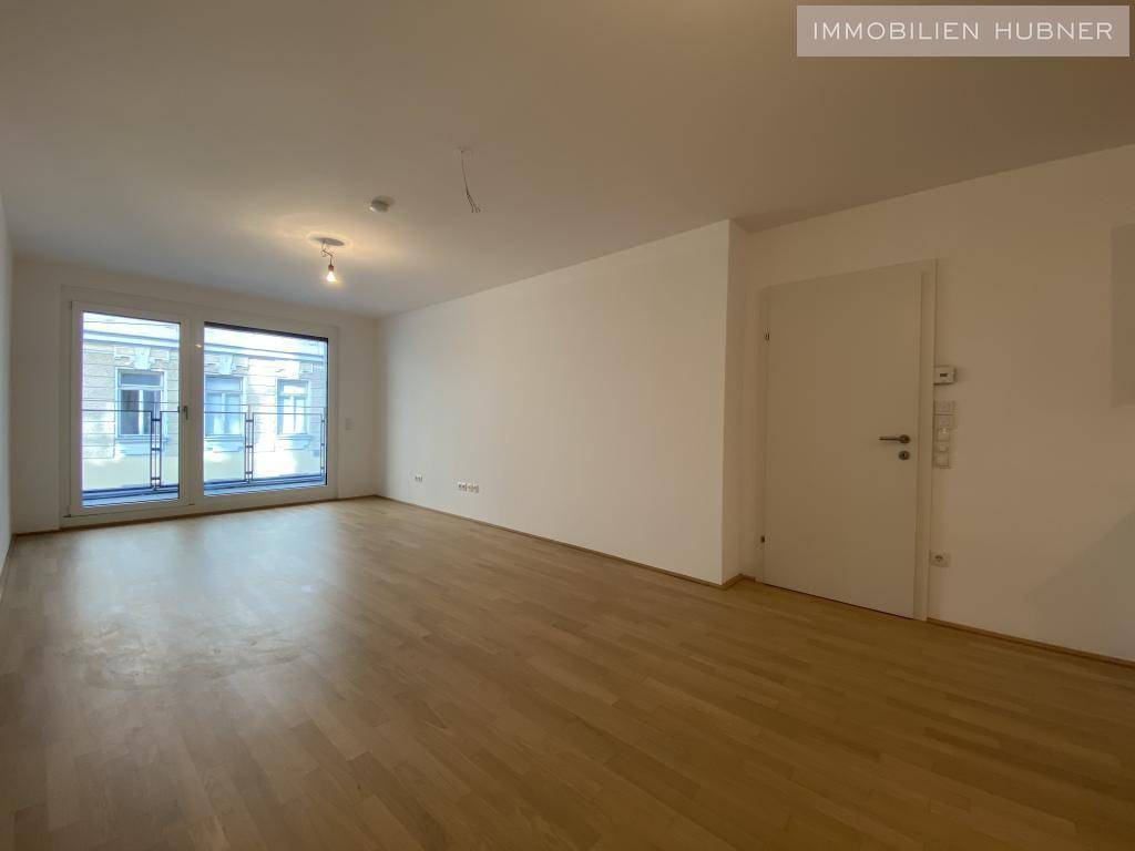 Heller Wohnbereich mit Parkettboden und großen Fenstern, die viel Tageslicht hereinlassen.