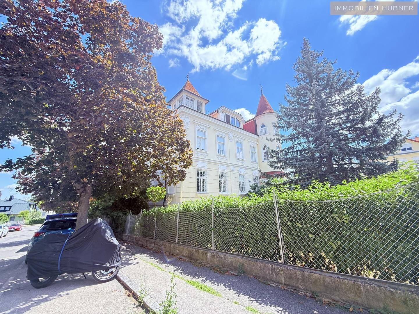 Historisches Gebäude mit markantem Turm und üppiger Vegetation in der Umgebung.