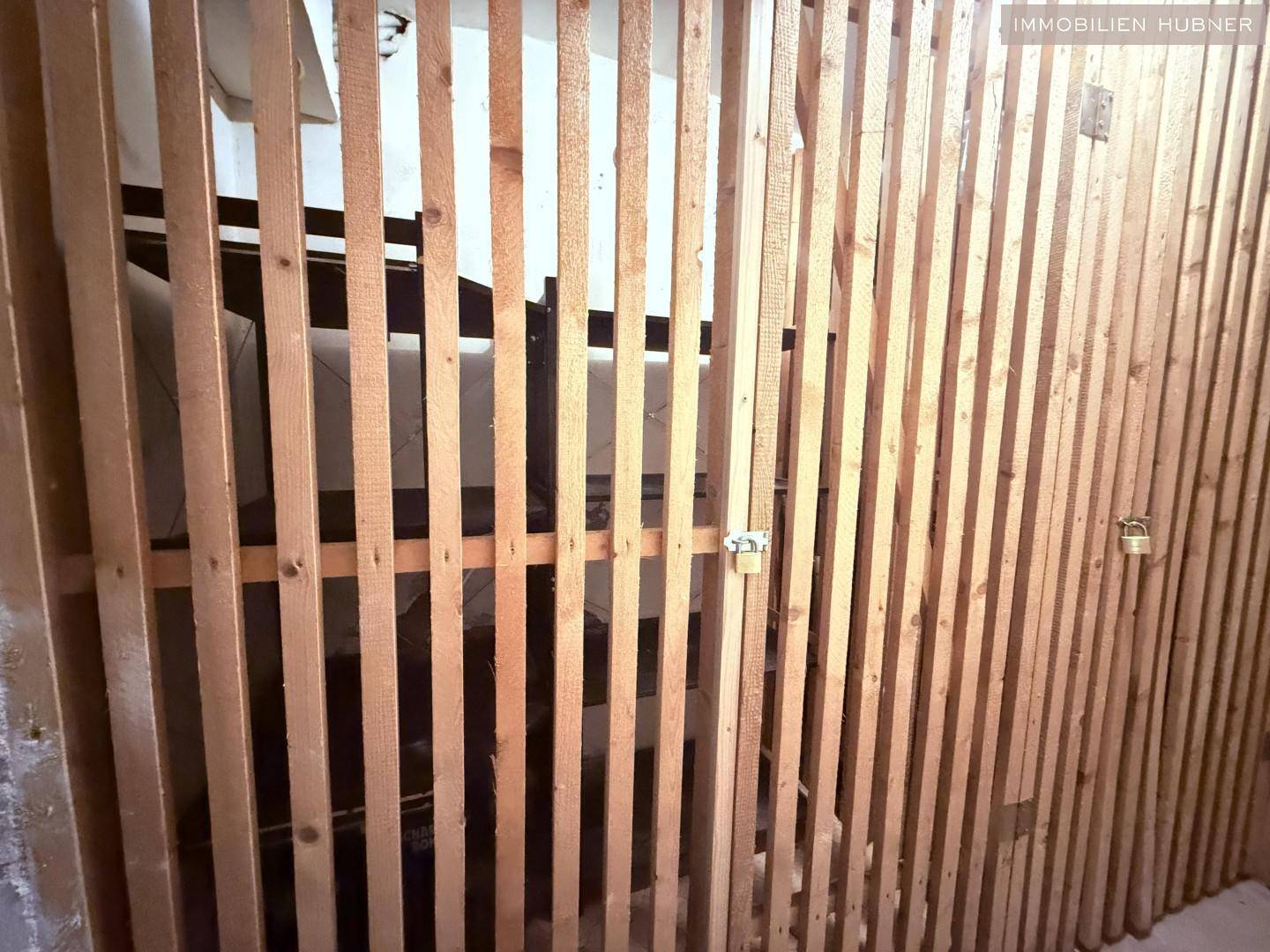 Nahaufnahme der Holzlattenwände eines Kellerabteils mit Vorhängeschlössern.