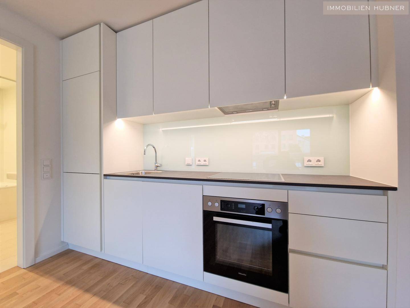 Moderne Einbauküche mit weißen Schränken, integriertem Backofen und heller Arbeitsplatte.