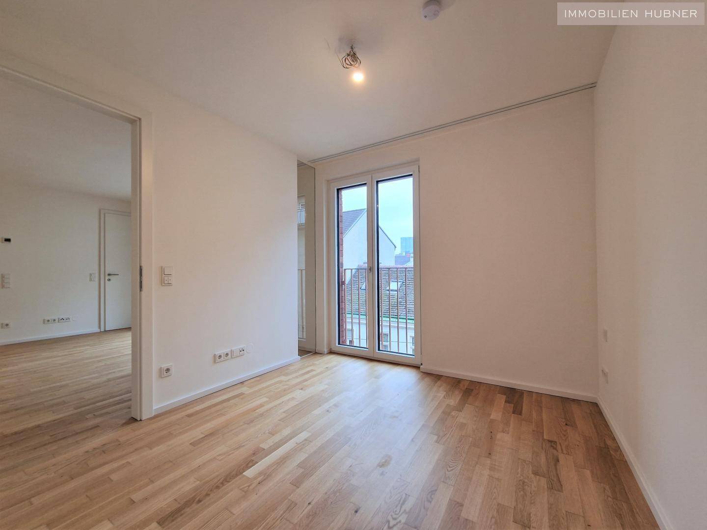 Helles Schlafzimmer mit Parkettboden und Zugang zu einem Balkon, bereit zur Einrichtung.