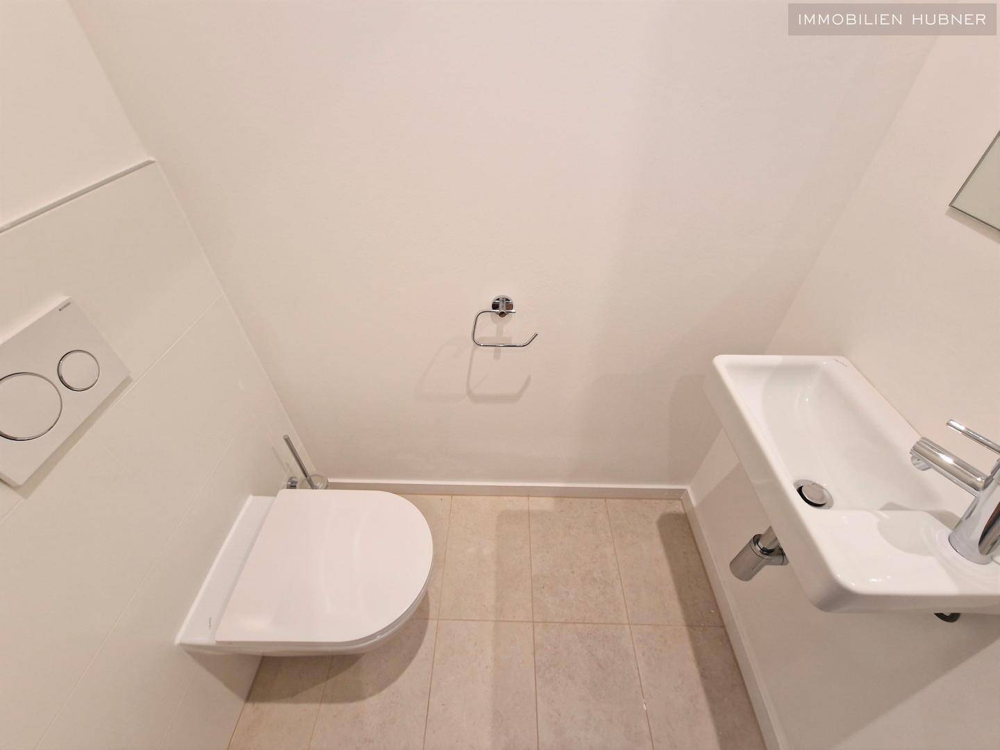 Separates WC mit wandhängender Toilette und kleinem Handwaschbecken, in modernem Design gehalten.