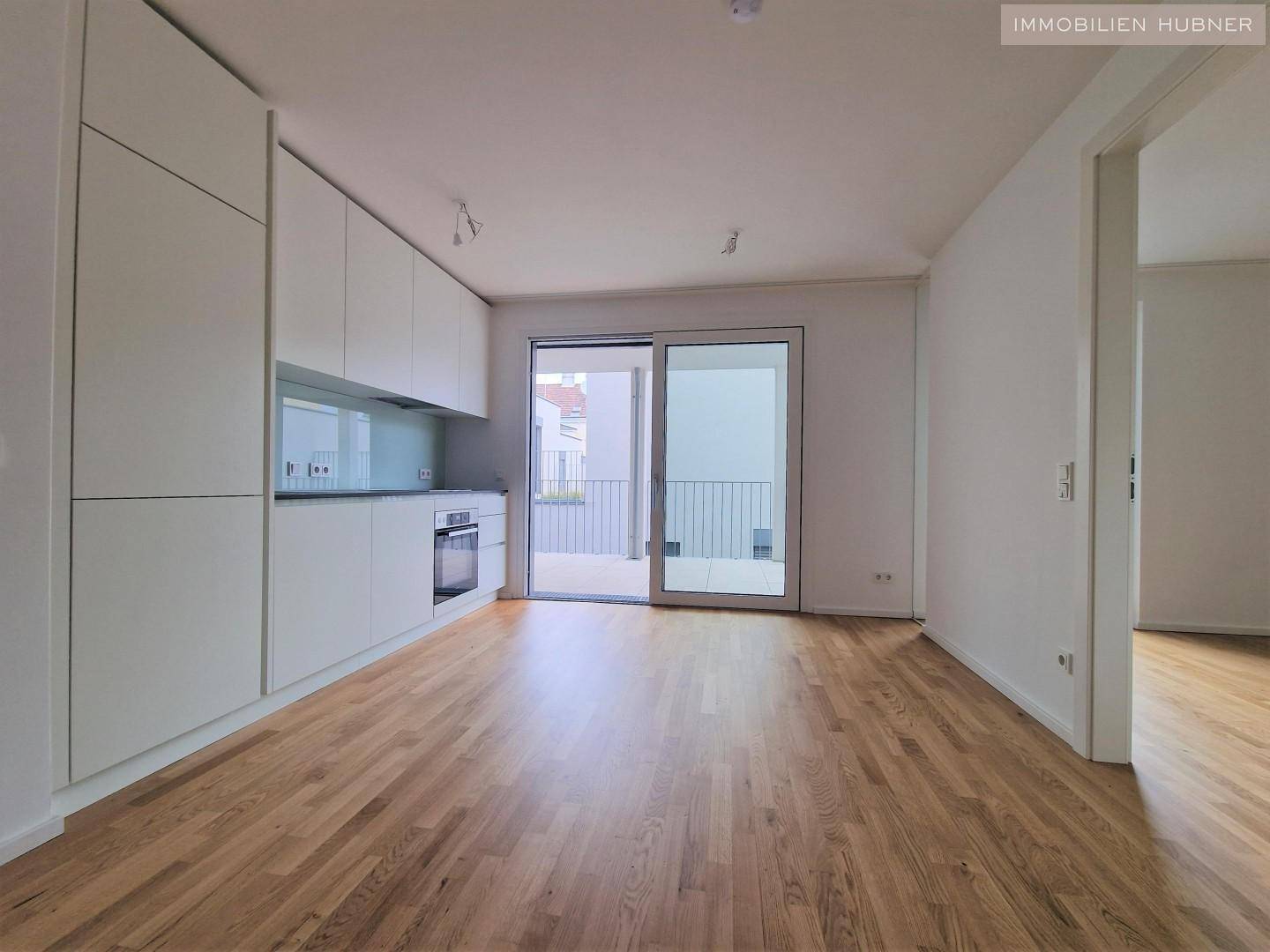 Moderner Wohnbereich mit integrierter Küche, Parkettboden und großem Schiebetürzugang zum Balkon.