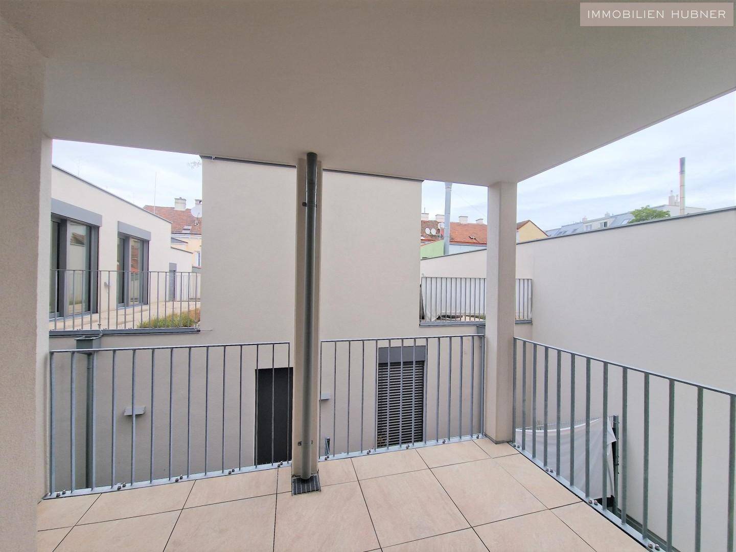 Überdachter Balkon mit Fliesenboden und Blick auf die umliegenden Gebäude, bietet einen geschützten Außenbereich.
