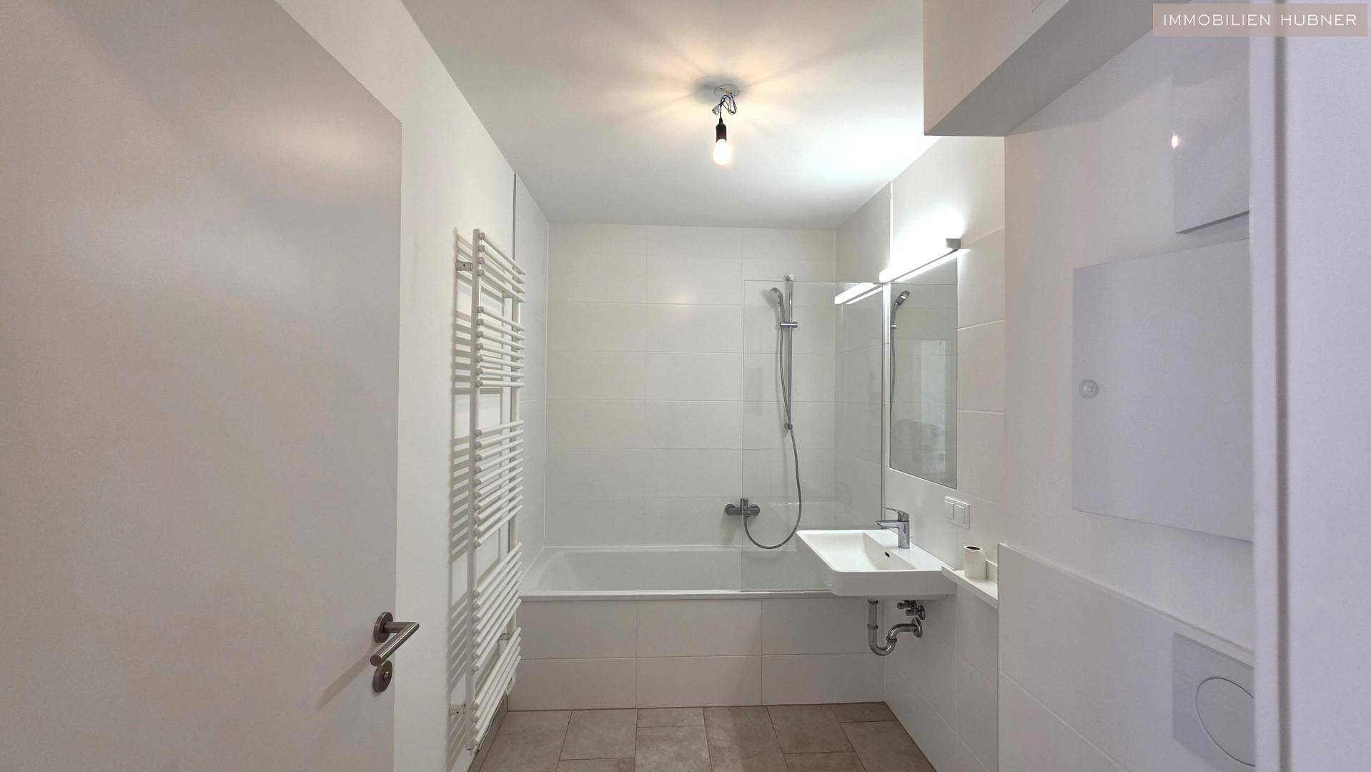 Modernes Badezimmer mit weißen Fliesen, Badewanne mit Duschfunktion und beheiztem Handtuchhalter.