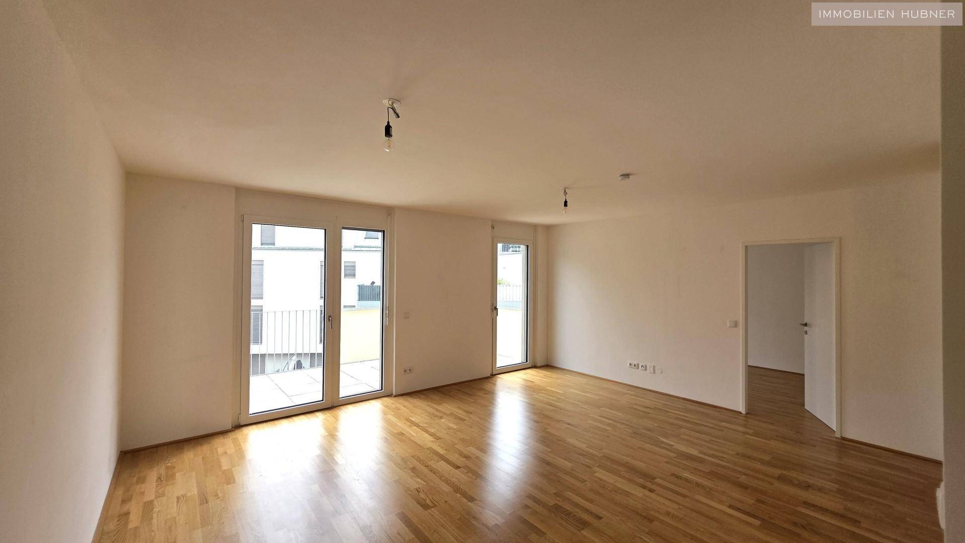Geräumiges Wohnzimmer mit hellem Parkettboden und direktem Zugang zum Außenbereich durch große Türen.