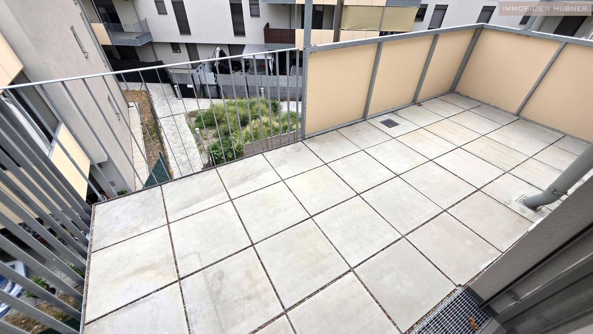 Gefliester Balkon mit Metallgeländer und Blick auf den begrünten Innenhof, ideal zum Entspannen.