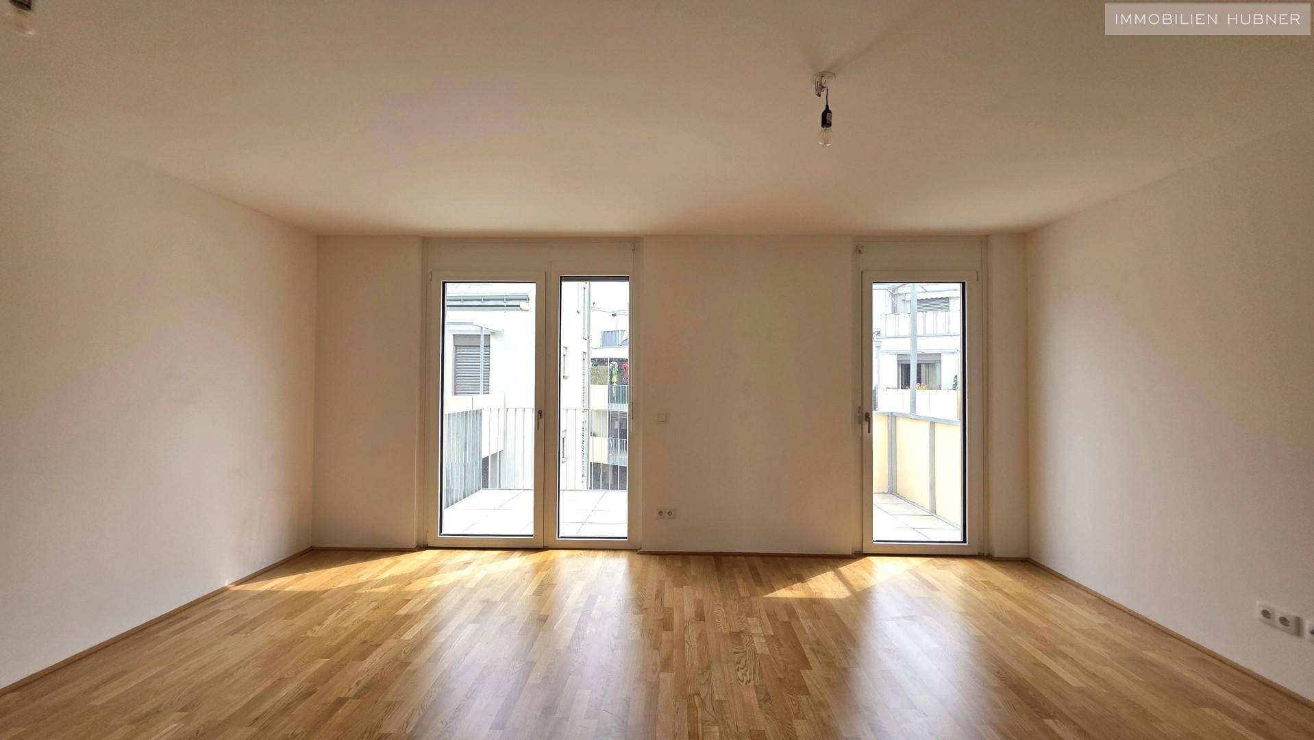 Helles und geräumiges Wohnzimmer mit Parkettboden und viel Tageslicht durch die Balkontüren.