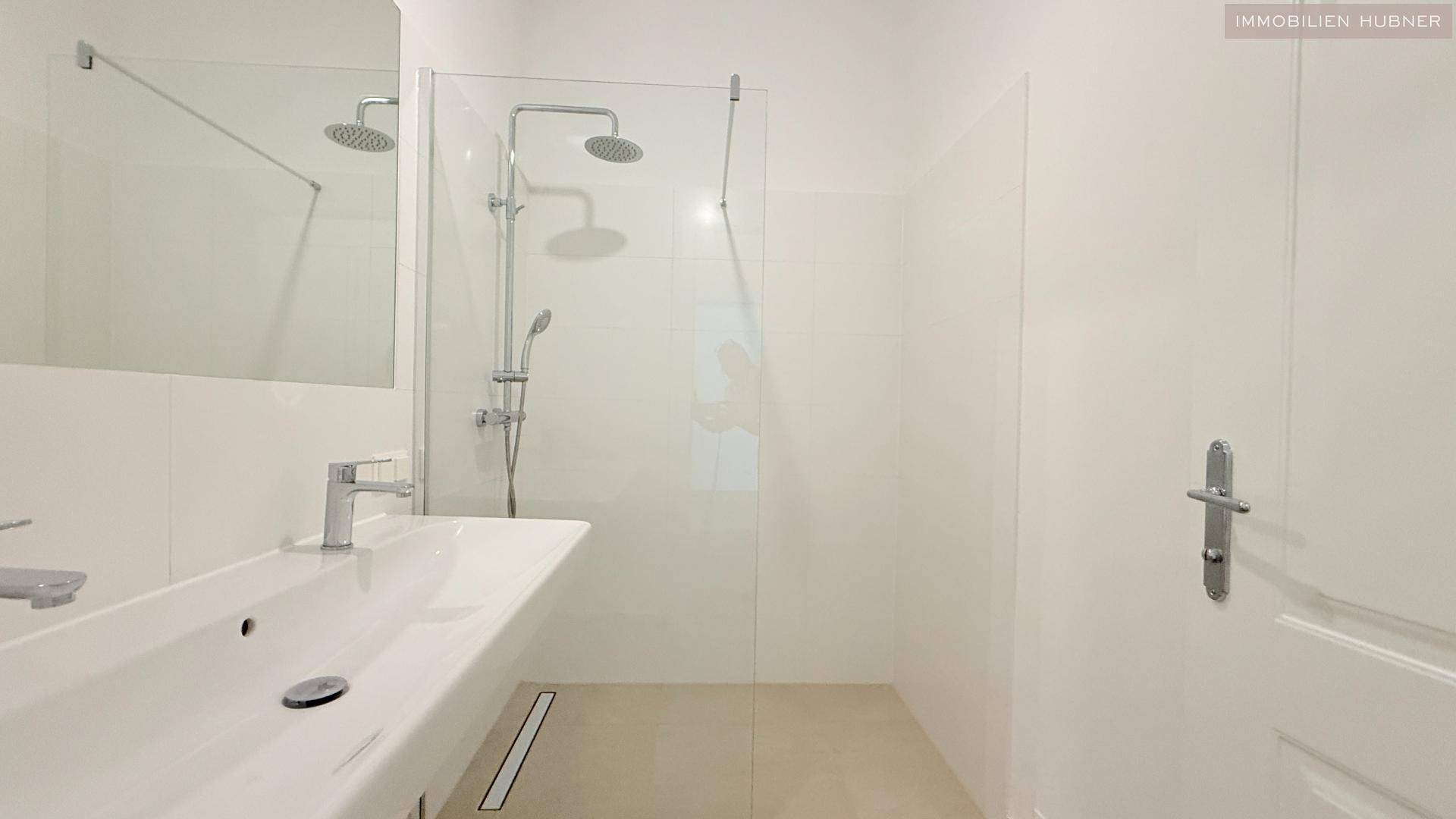 Modernes Badezimmer mit begehbarer Dusche, Einzelwaschbecken und großen weißen Fliesen.