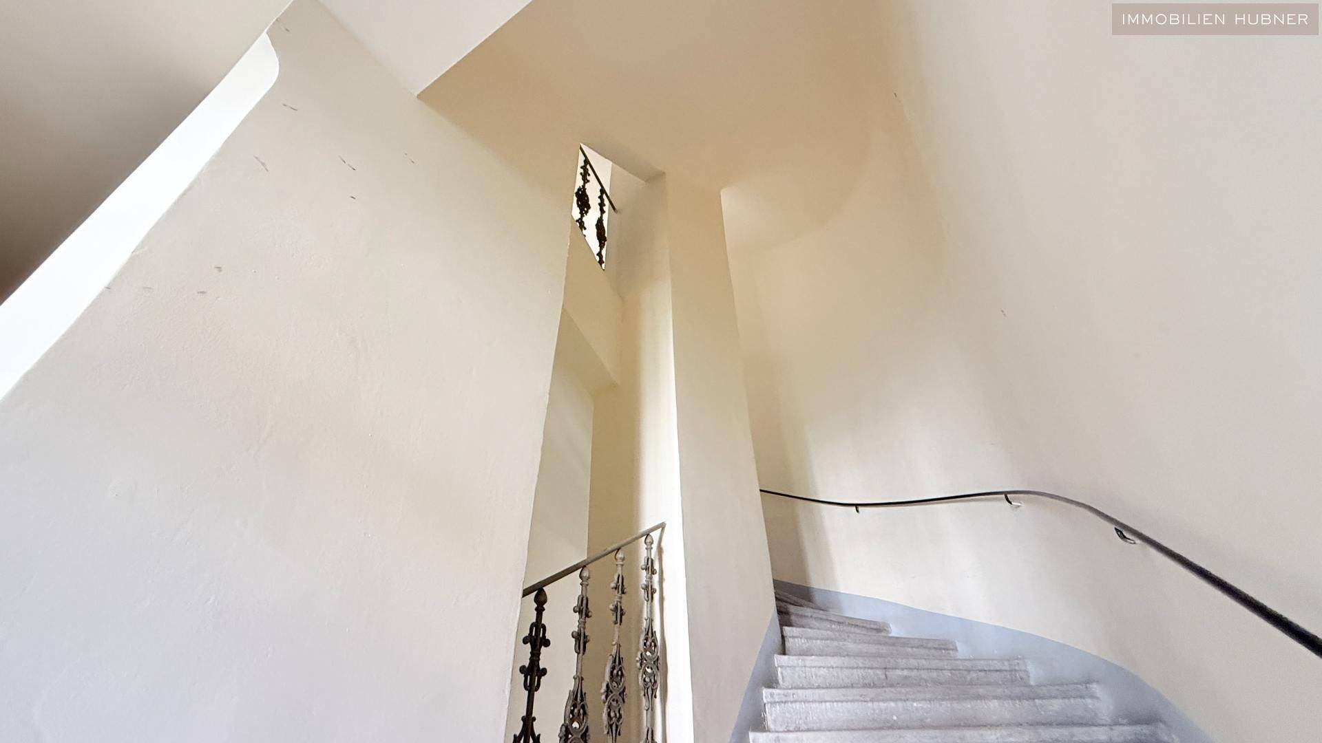 Elegantes Treppenhaus mit Steinstufen und einem kunstvollen Metallgeländer in einem Altbau.