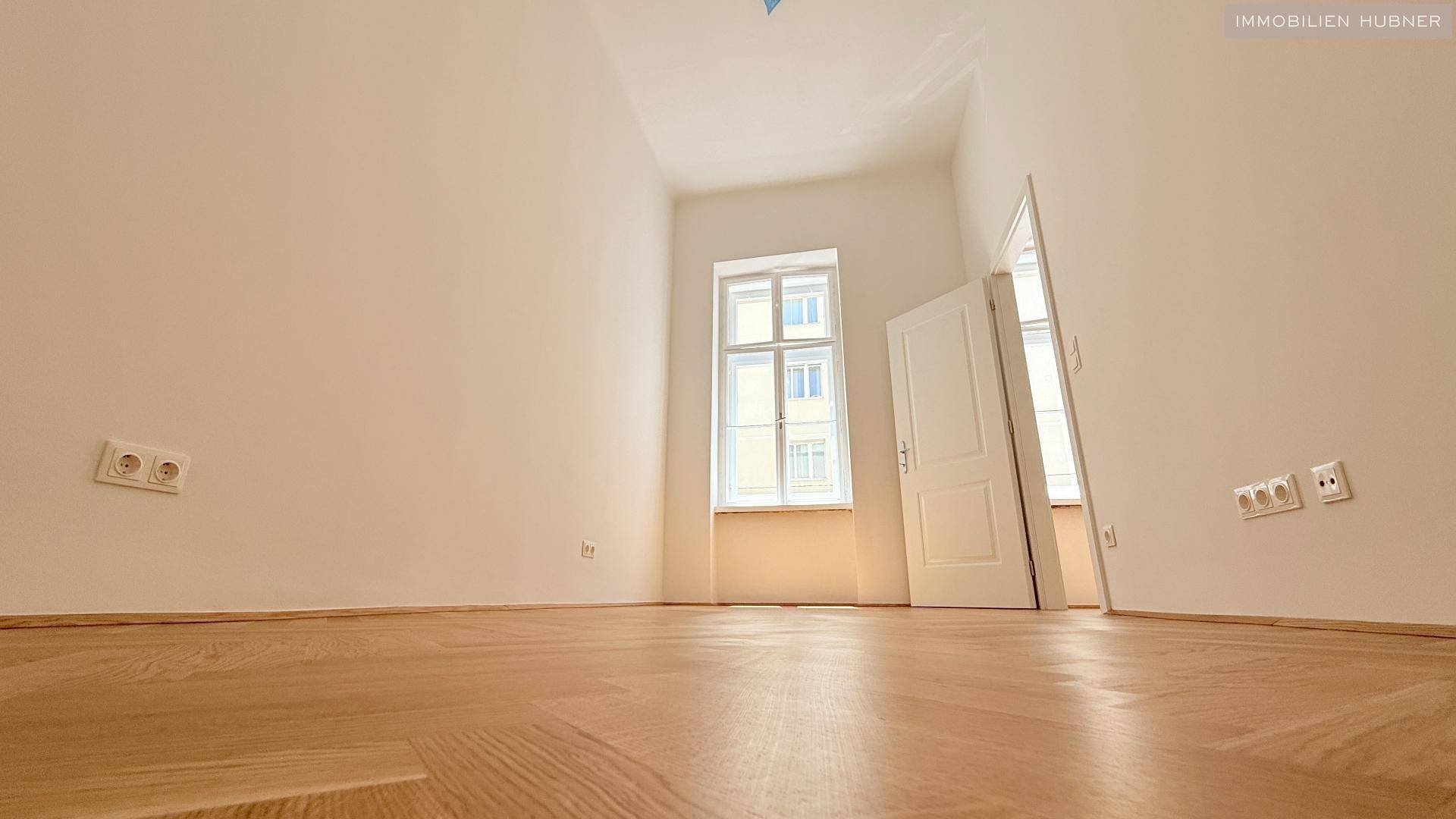 Ruhiges Schlafzimmer mit Fischgrätparkett und einem großen Fenster, bietet viel Tageslicht.