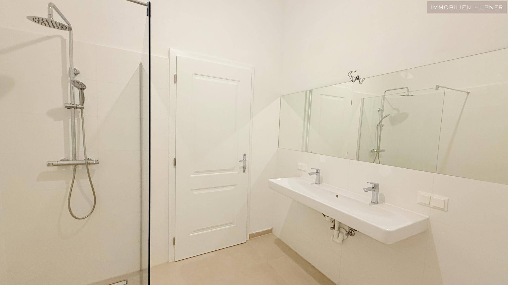 Geräumiges Badezimmer mit Doppelwaschbecken und moderner begehbarer Dusche mit Regenduschkopf.