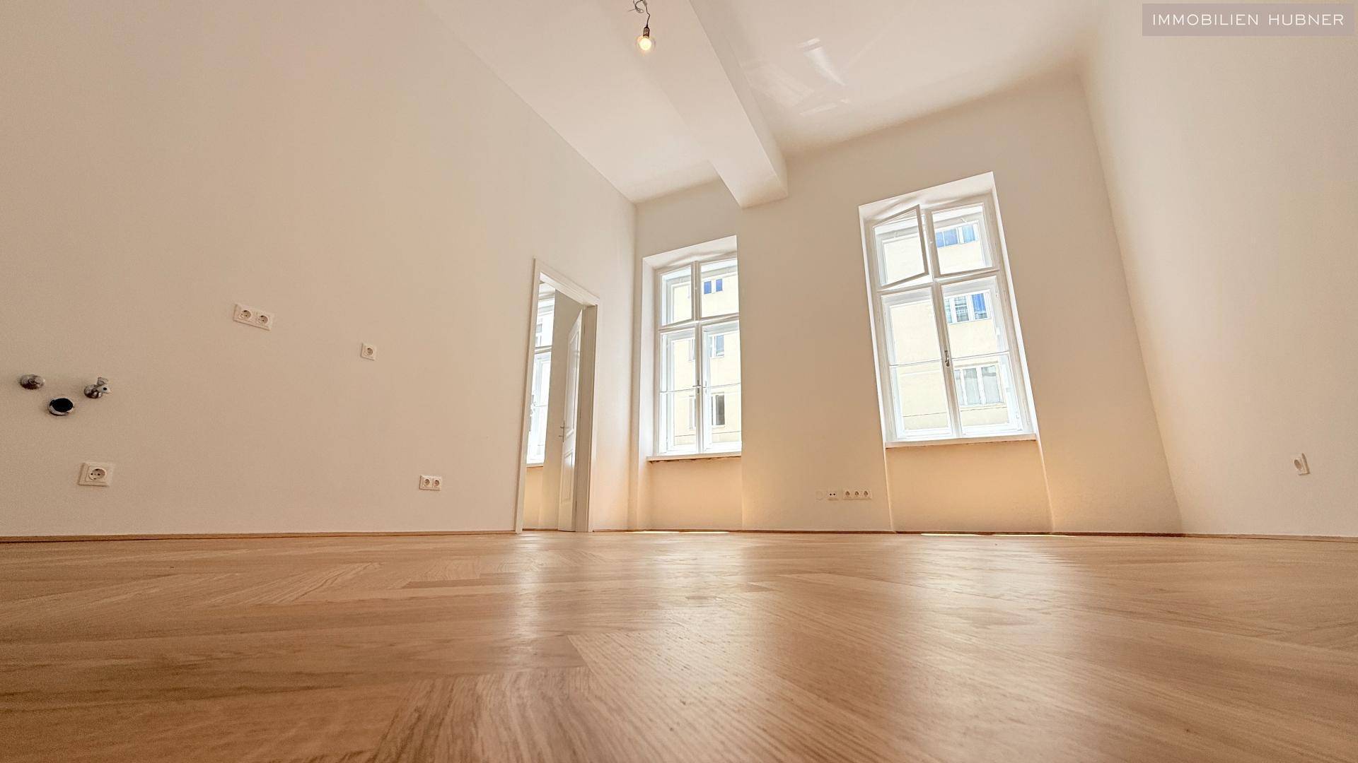 Lichtdurchflutetes Zimmer mit elegantem Fischgrätparkett und hohen Decken, bietet viel Raumgefühl.