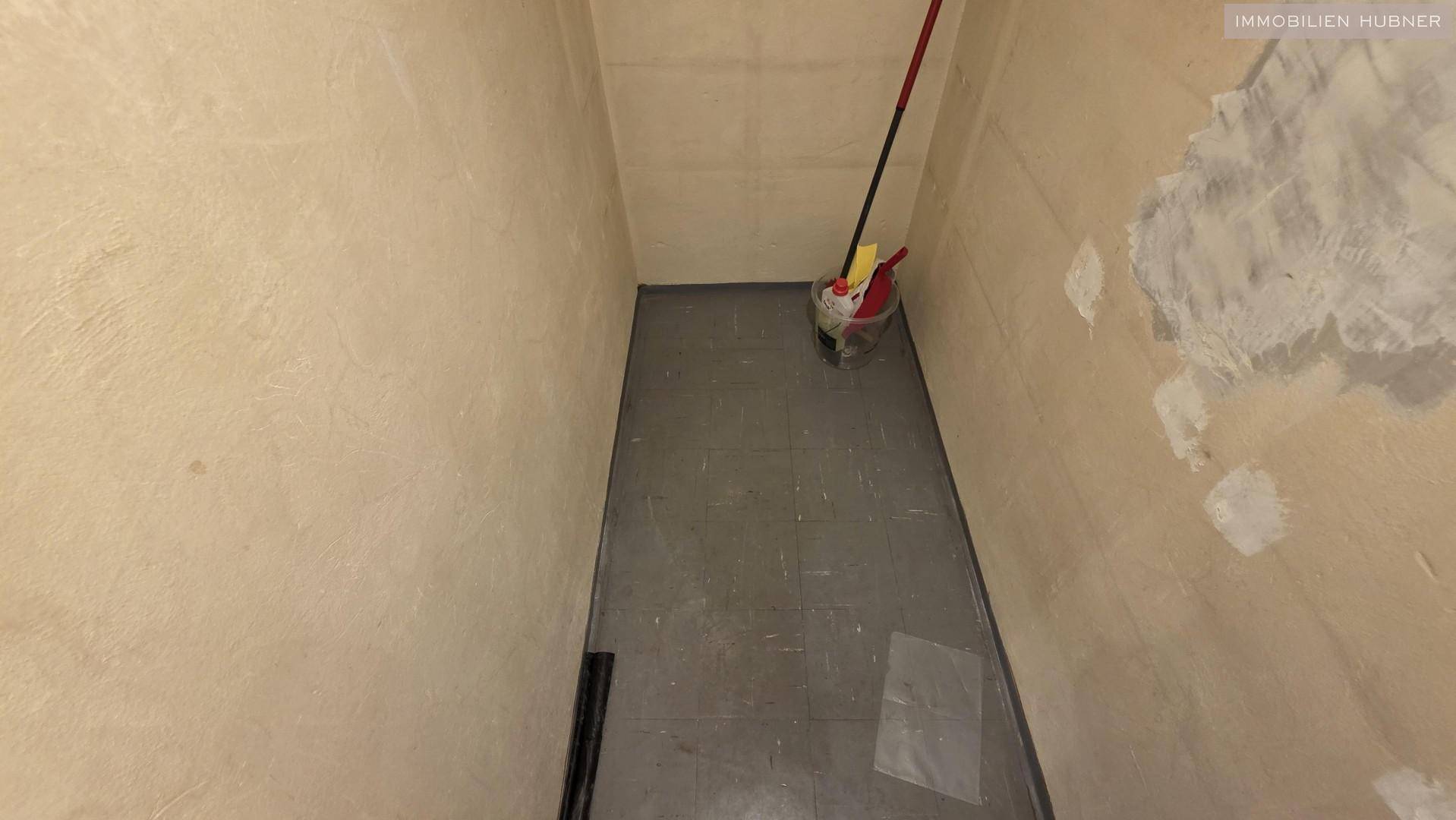 Schmaler Hauswirtschaftsraum mit grauen Fliesen und beige gestrichenen Wänden, ideal für Reinigungsutensilien.