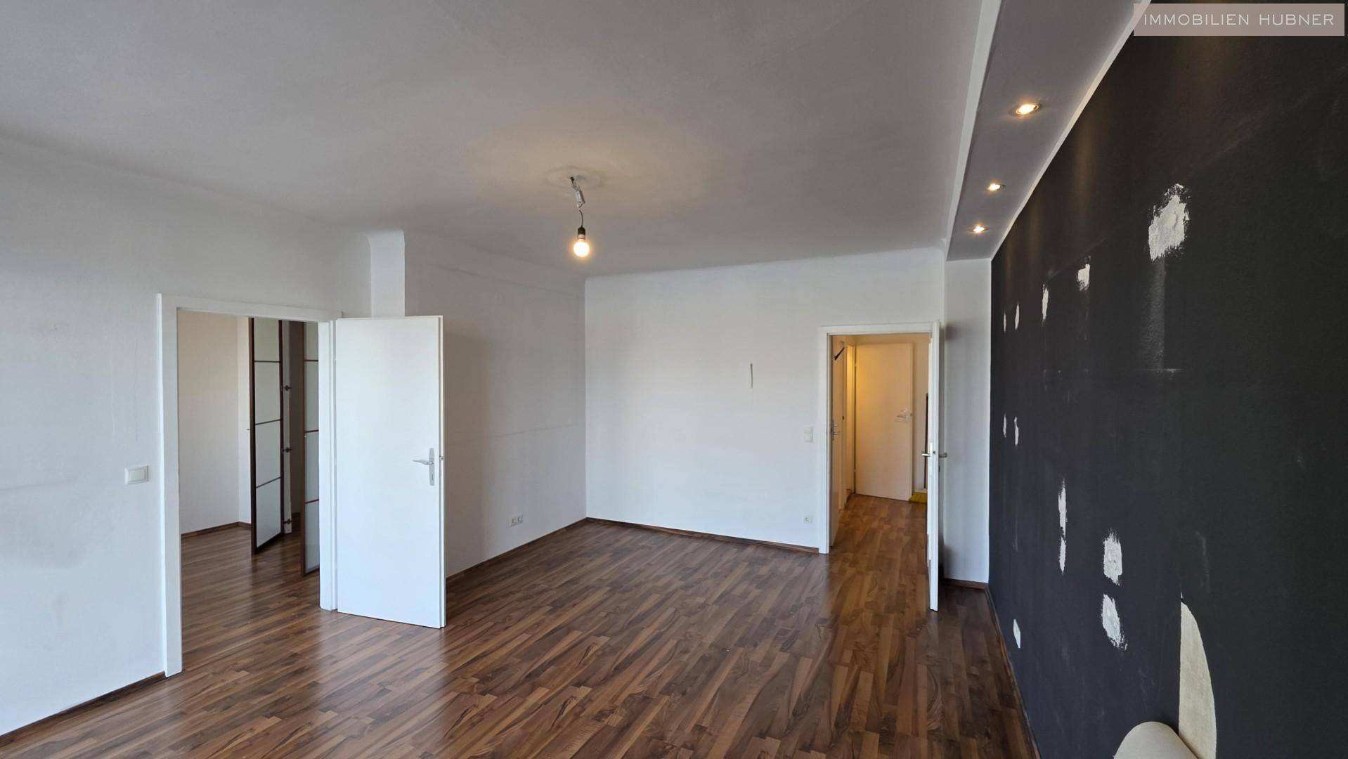 Weitläufiger Wohnbereich mit dunkler Akzentwand, Holzboden und mehreren Türöffnungen.