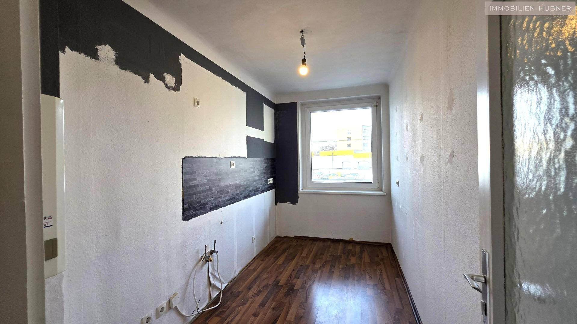 Raum mit Holzboden und Fenster, vorbereitet für die Installation einer Küche oder als Hauswirtschaftsraum.