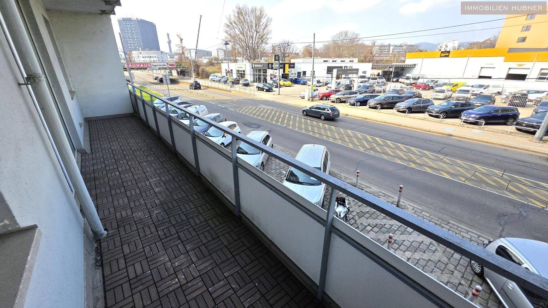 Geräumiger Balkon mit Blick auf eine belebte Straße und umliegende Geschäftsgebäude.
