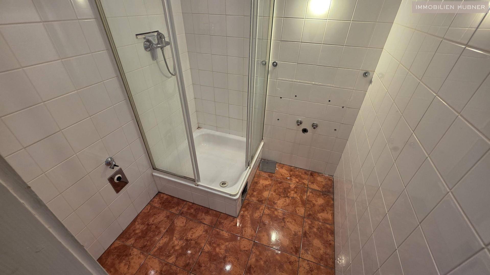 Badezimmer mit Duschkabine, weißen Wandfliesen und braunen Bodenfliesen.