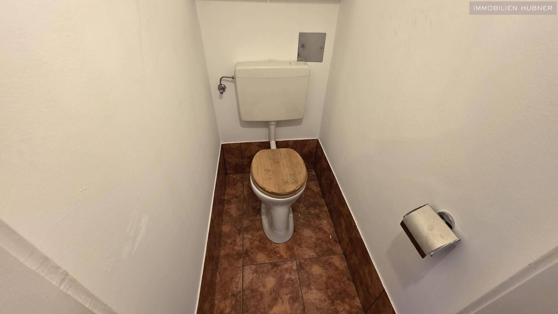 Separates WC mit Toilette und braunen Bodenfliesen, funktional und kompakt gestaltet.