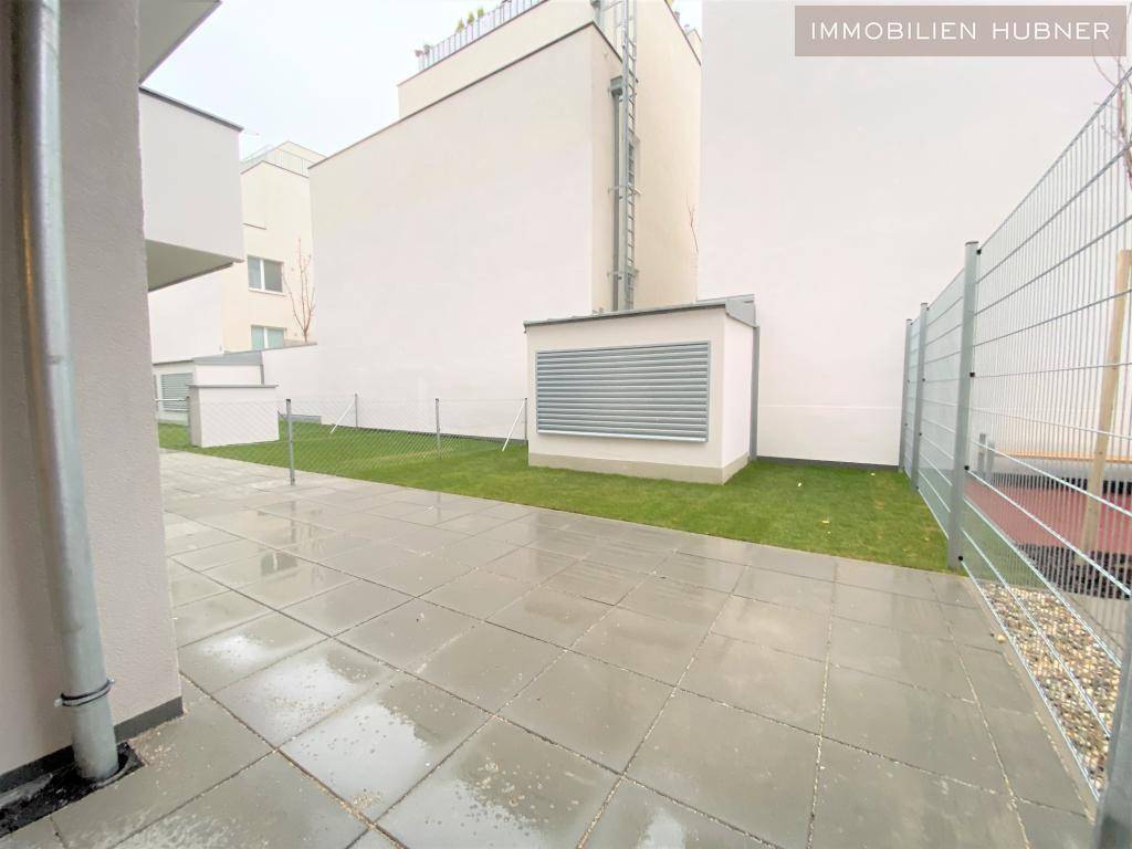 Gepflasterte Terrasse mit angrenzender Rasenfläche und Blick auf die modernen Gebäude.