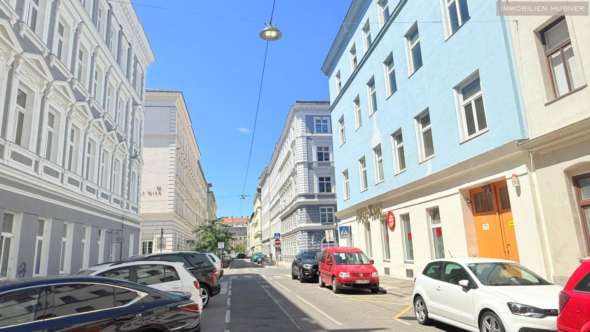 Ruhige Wohnstraße mit parkenden Autos und historischen Gebäuden unter blauem Himmel.