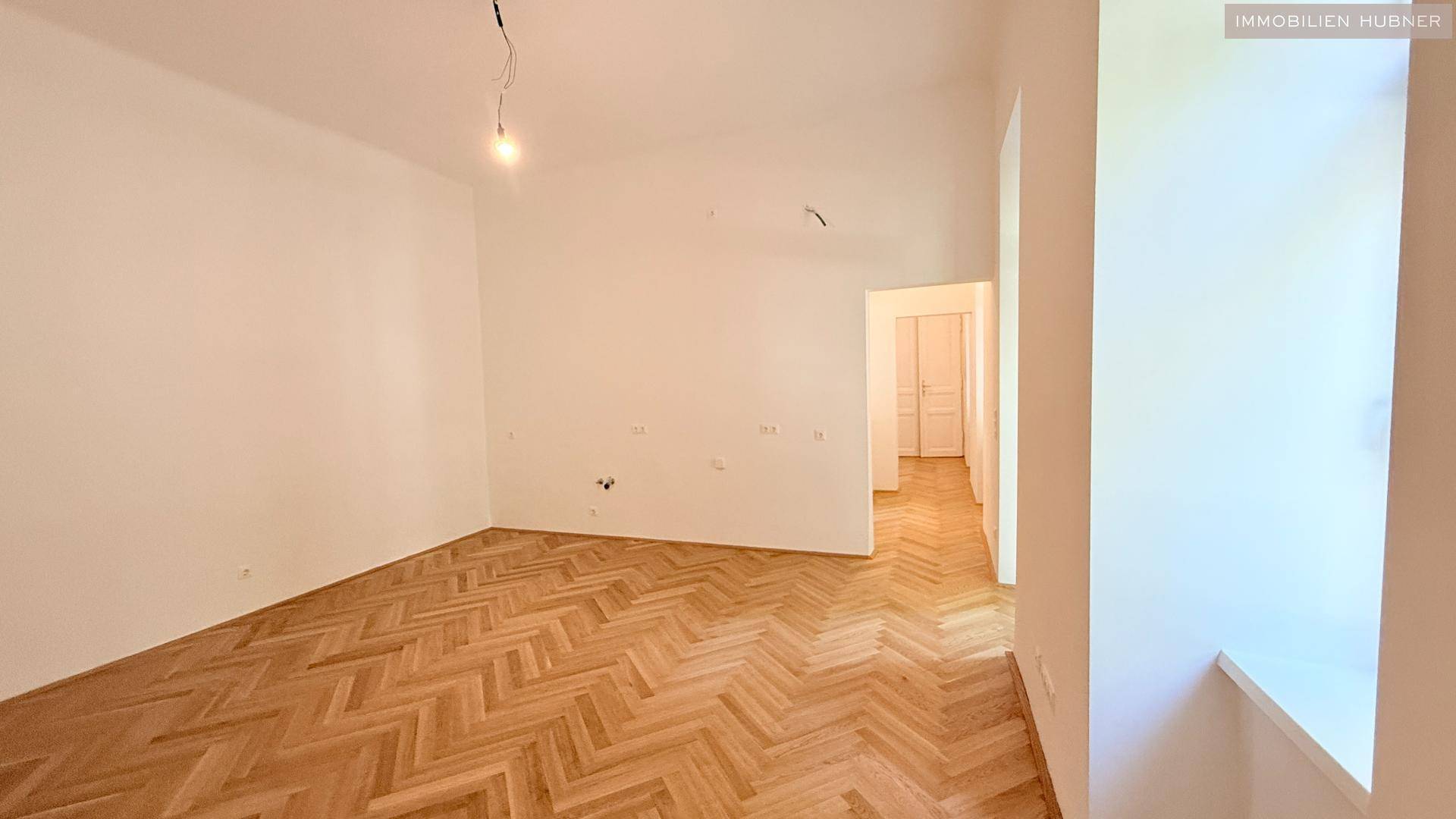 Geräumiges Zimmer mit Fischgrätparkett und Blick in den angrenzenden Flur mit weißen Türen.