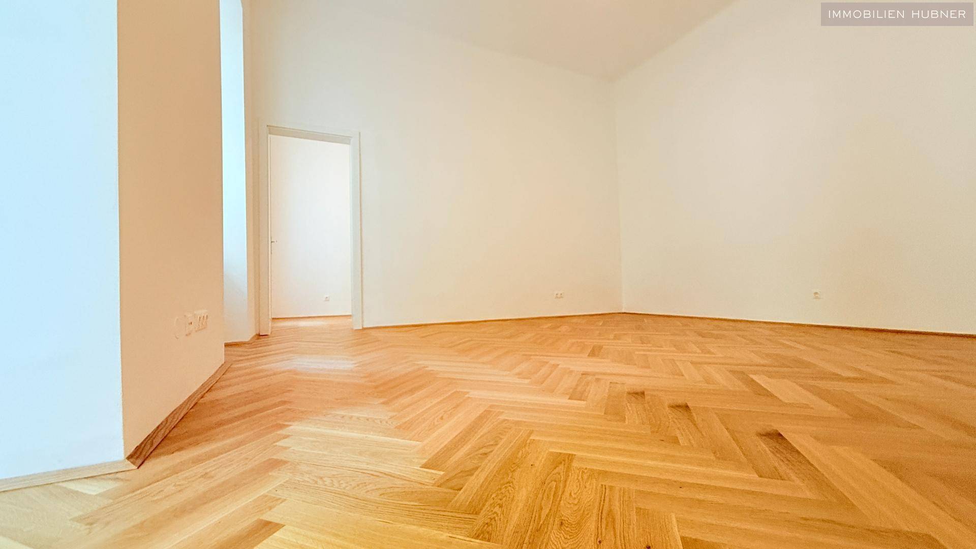 Leeres Zimmer mit hellem Fischgrätparkett und weiß gestrichenen Wänden, bereit zur Gestaltung.