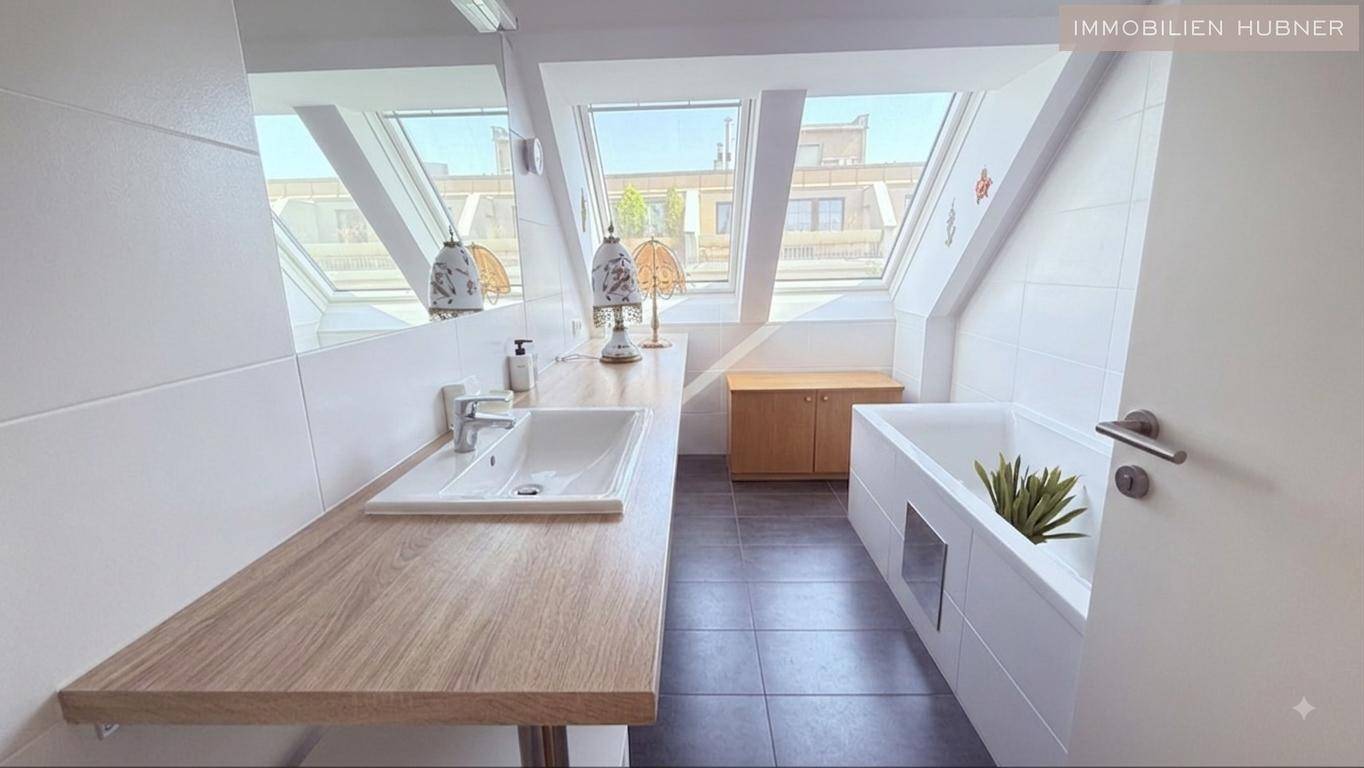 Helles Badezimmer mit Badewanne, Holzwaschtisch und Dachfenstern, die viel Tageslicht hereinlassen.