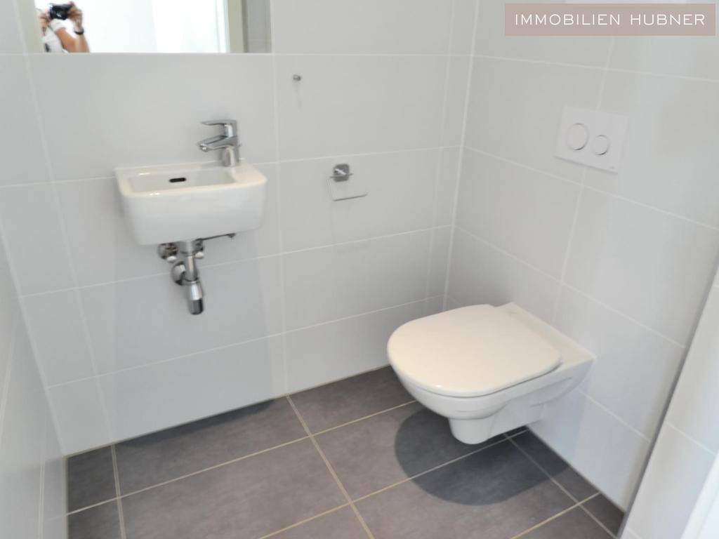 Modernes Gäste-WC mit wandhängender Toilette, kleinem Waschbecken und hellen Fliesen.