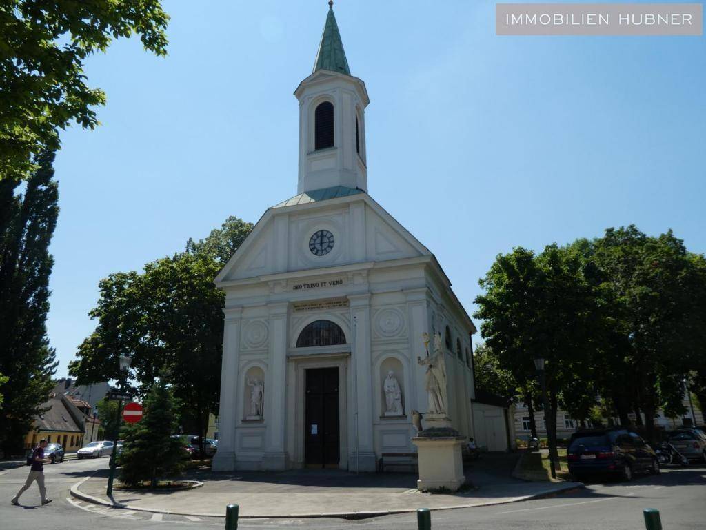 Historisches Kirchengebäude auf einem Stadtplatz, umgeben von Bäumen und einer ruhigen Umgebung.