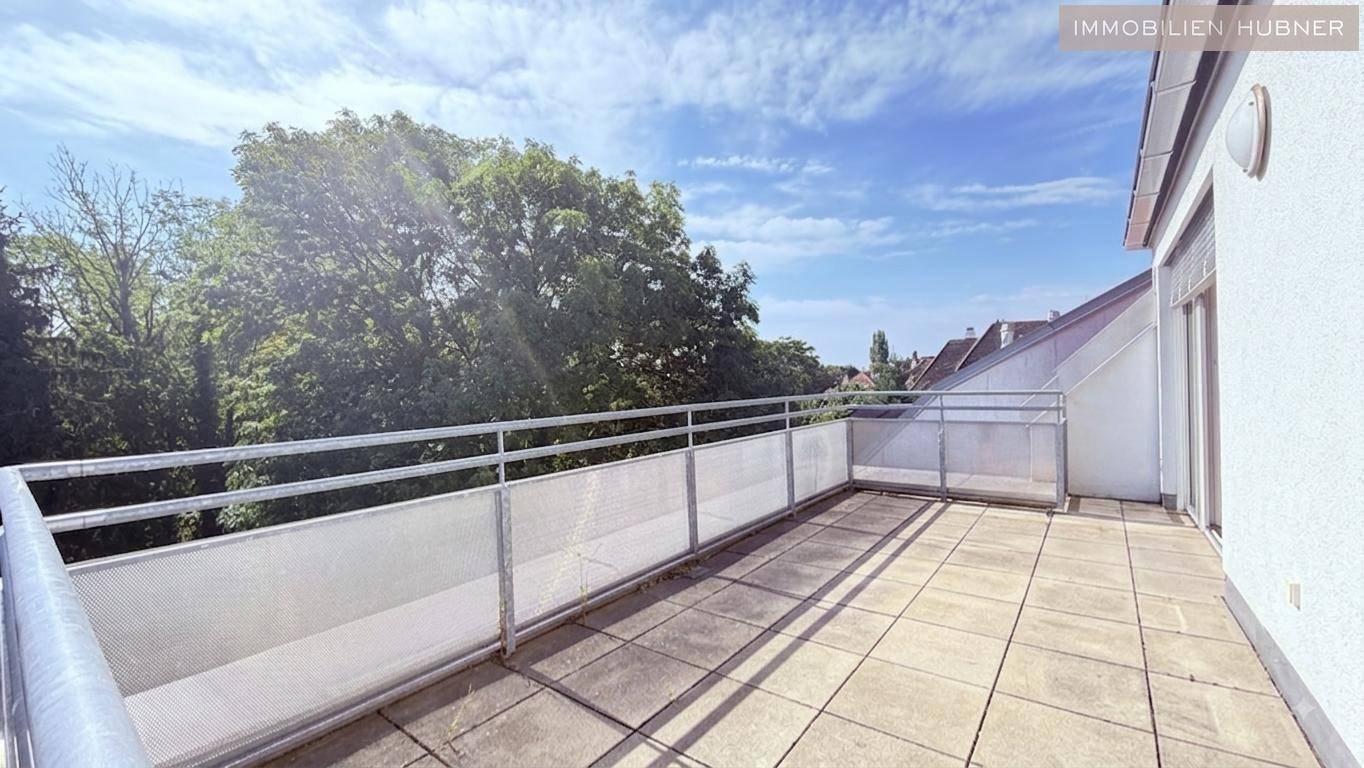Sonniger Balkon mit Fliesenboden und Blick ins Grüne, umgeben von Bäumen und Wohngebäuden.