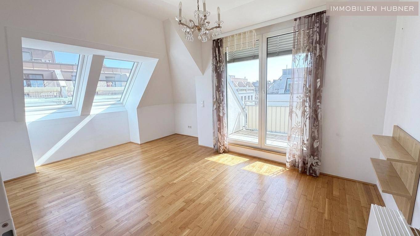 Geräumiges Schlafzimmer mit Parkettboden, Dachschrägen und Zugang zu einem sonnigen Balkon.