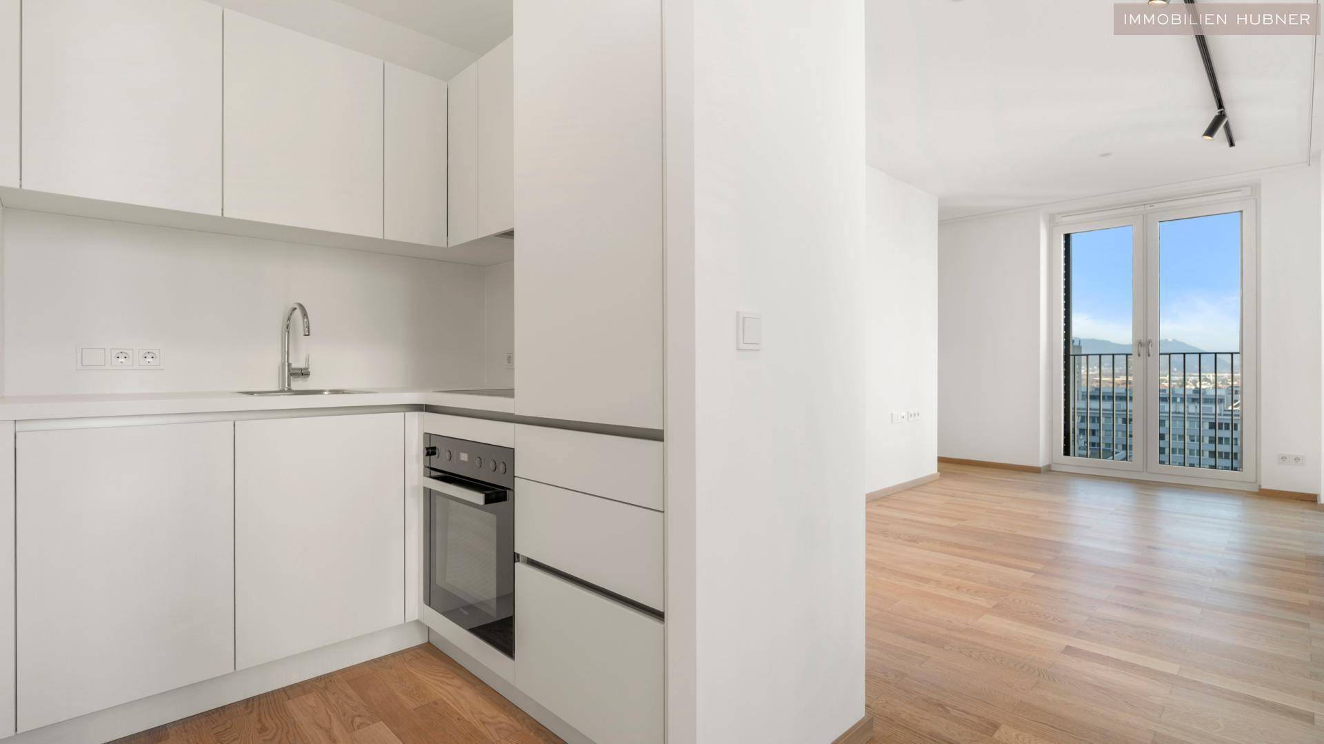 Moderne, helle Küche mit weißen Schränken und integriertem Backofen, offen zum Wohnbereich.