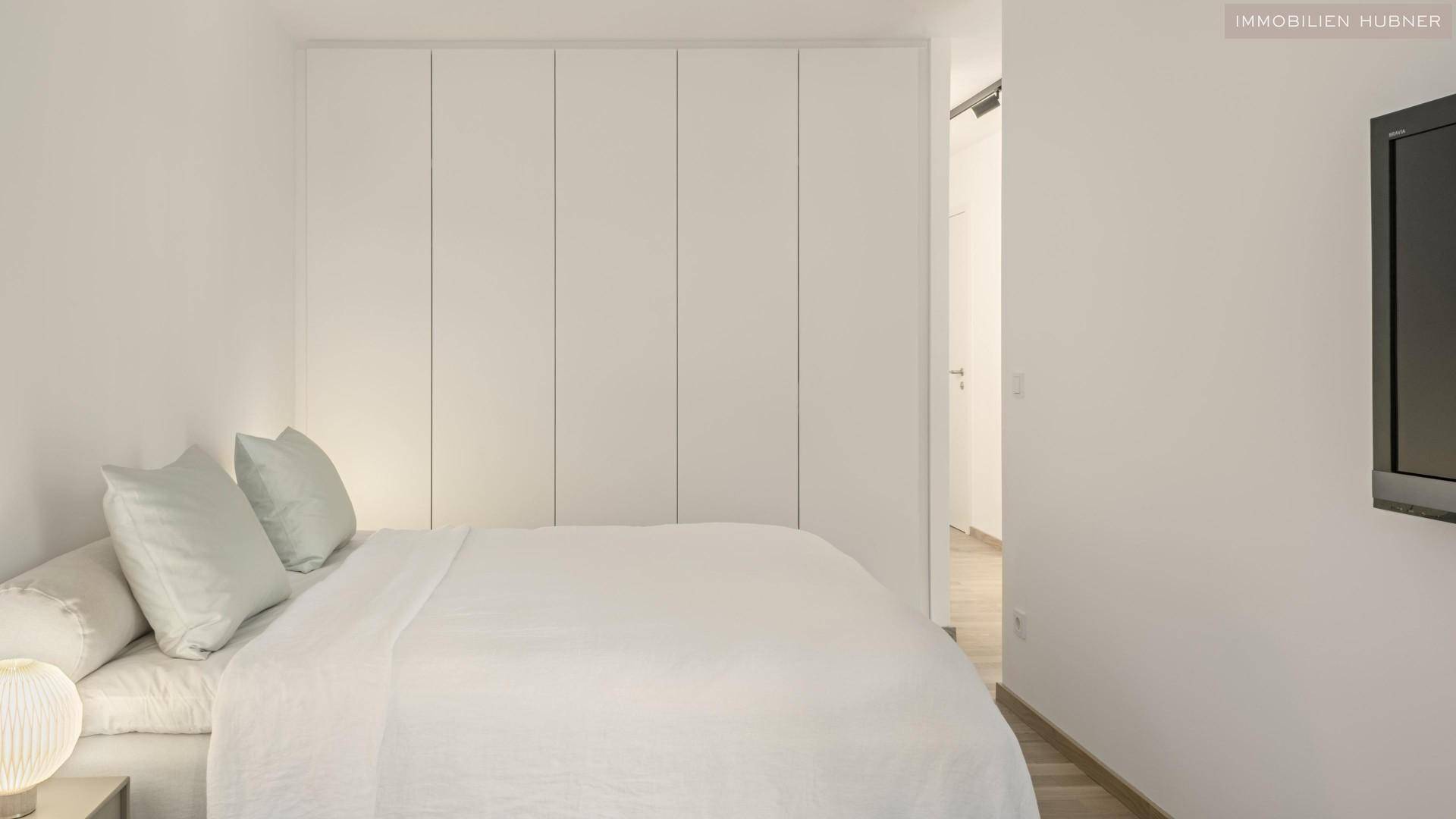 Gemütliches Schlafzimmer mit weißem Bett, Einbauschränken und minimalistischer Einrichtung.