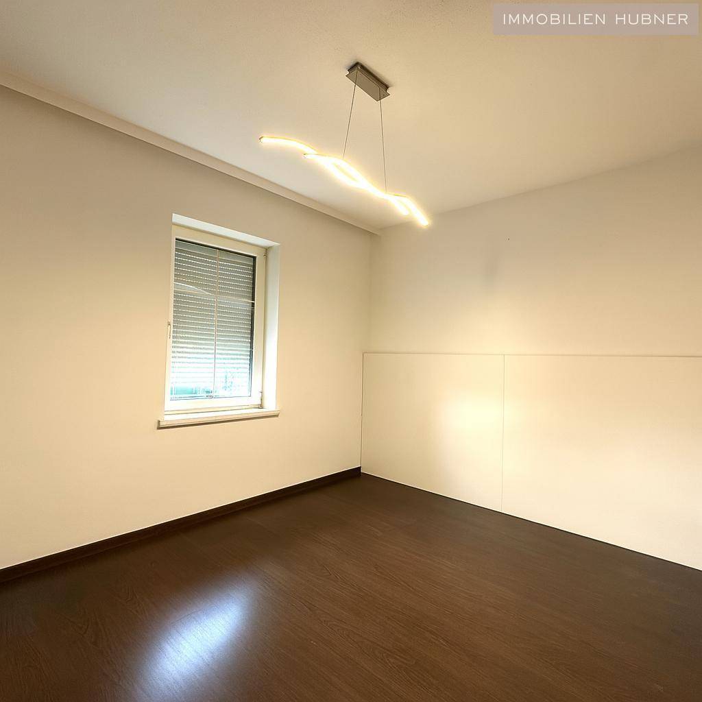 Zimmer mit dunklem Laminatboden, Fenster und moderner Deckenleuchte.