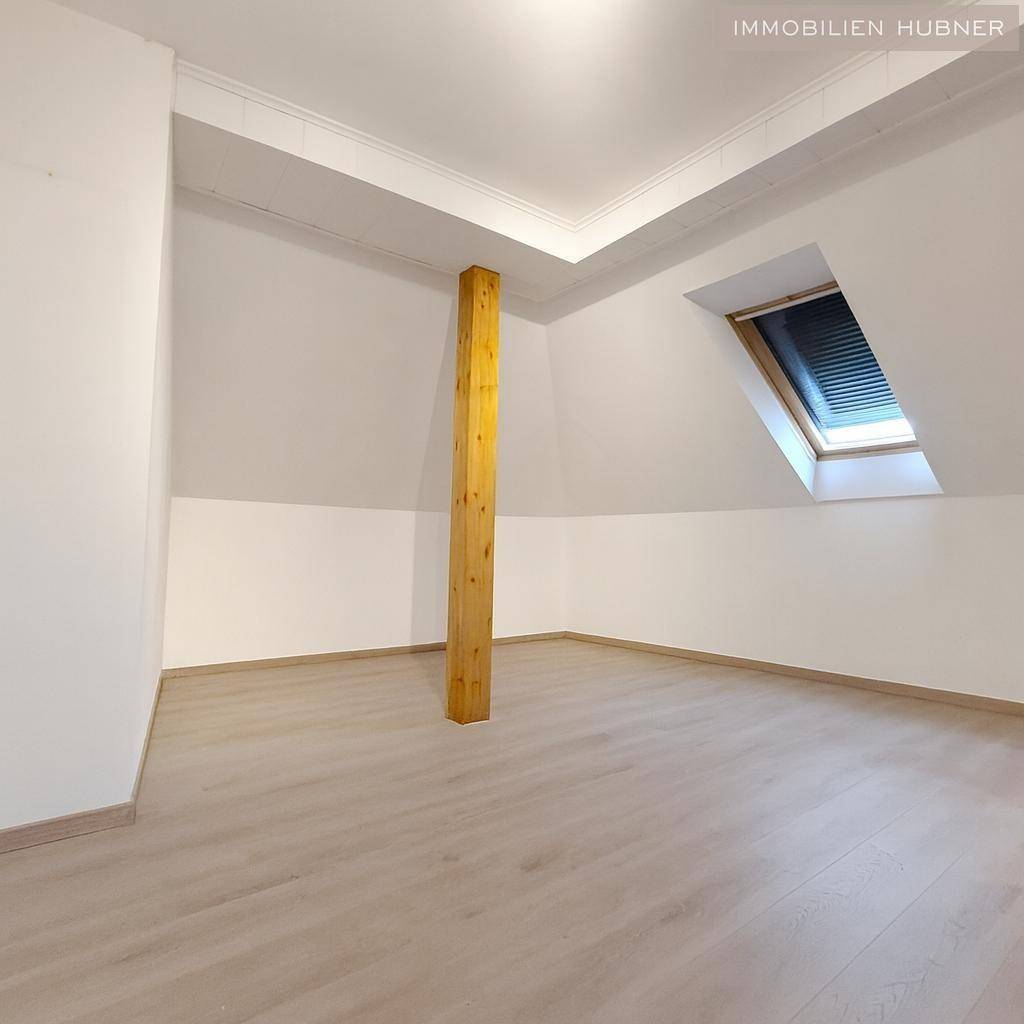 Helles Dachzimmer mit Holzbalken, Laminatboden und Dachfenster.