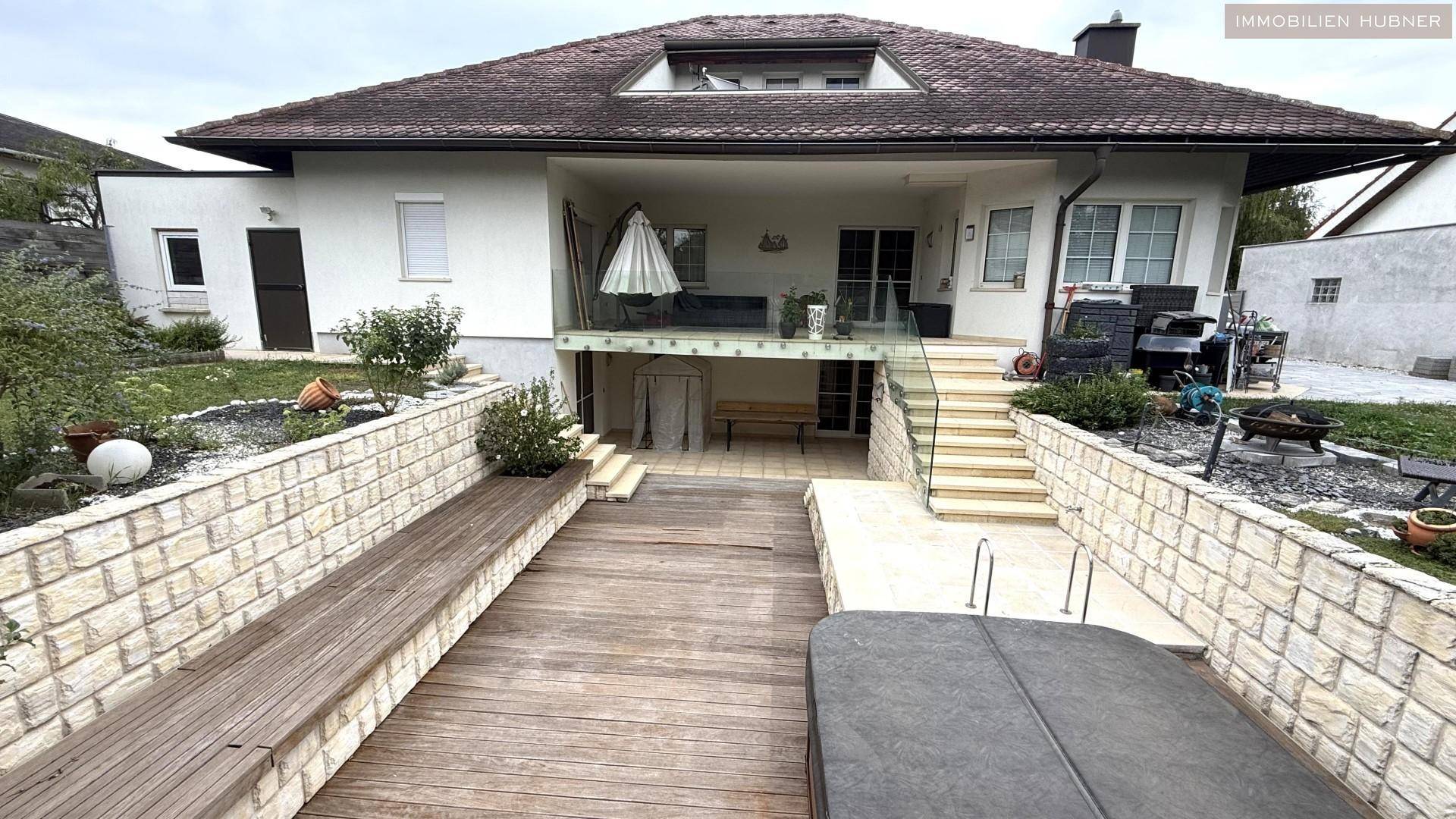 Rückansicht des Hauses mit Garten, Terrasse, Whirlpool und Steinmauern.