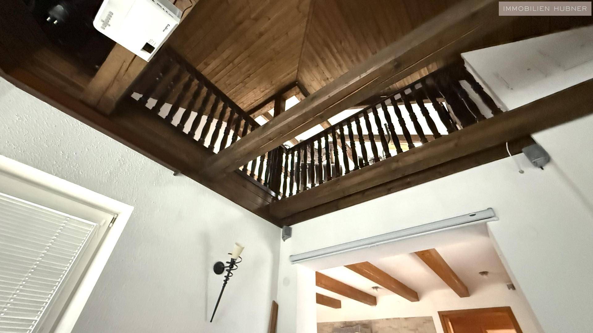 Holztreppe mit Geländer und Holzbalkendecke, die verschiedene Ebenen verbindet.