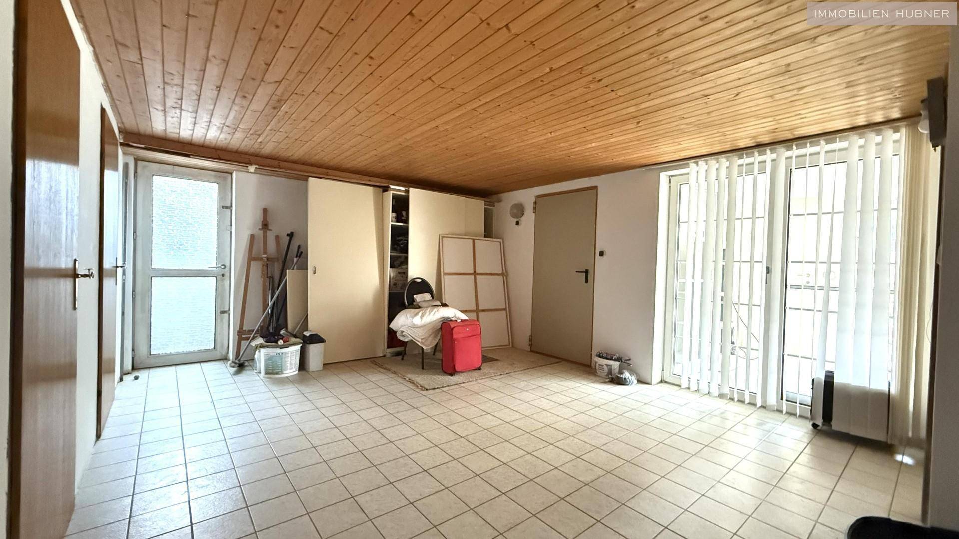 Vielseitiger Raum mit Fliesenboden, Holzdecke und Zugang zum Außenbereich.