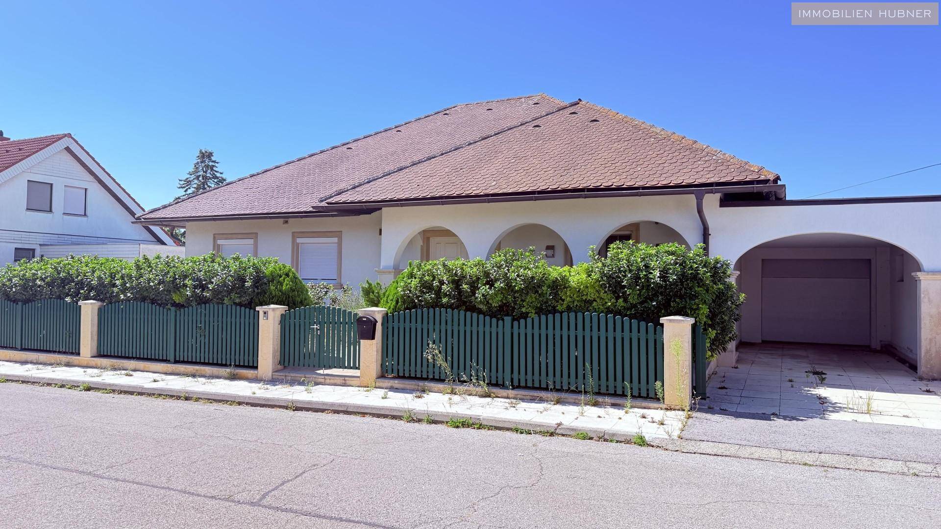 Vorderansicht des Hauses mit Zaun, Vorgarten und überdachtem Garagenzugang.
